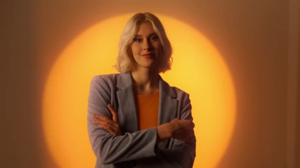 スタジオでオレンジ色の壁を越えて腕をポーズジャケットのブロンドのエレガントな女性 ファッション ショットのコンセプト — ストック動画