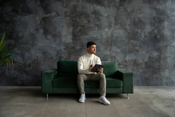 留胡子的设计师拿着平板电脑 望着阁楼客厅 年轻的有创造力的人坐在绿色的沙发上 工作场所设计人员概念 — 图库照片