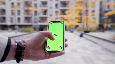 Açık havada Chromakey akıllı telefon kullanarak haberlere bakan sosyal bir adamın yakın çekimi. Şehirdeki kentsel sokağa karşı yeşil ekran model akıllı telefon kullanan insanlar
