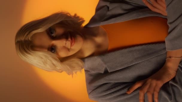 オレンジ色のスタジオの背景の上にポーズジャケットの肖像若いエレガントな女性の垂直ビデオ ファッションスタジオのショットコンセプト 肖像画 — ストック動画