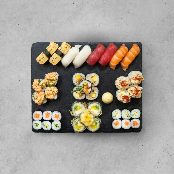 大盘寿司和蛋黄酱在灰色石桌的特殊黑色盘子里滚着 餐馆里的饭菜味道很好 日本菜的概念 带有复制空间的顶部视图 — 图库照片