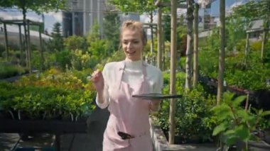 Beyaz önlüklü kadın bahçıvan ev stüdyosundaki açık hava bahçesinde çalışıyor. Kadın seraya su boşaltma sistemi kurmak için tablet bilgisayar kullanıyor, sayıyor, dans ediyor