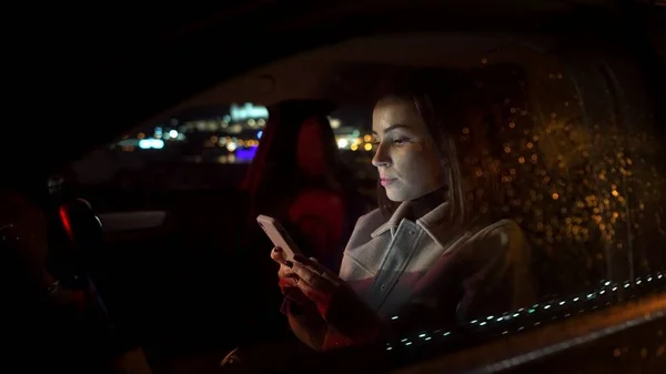 Şoförde akıllı telefon kullanan ciddi bir iş kadını gece lüks bir arabada işten eve giderken oturur. Neon ışıklı şehir caddesi 