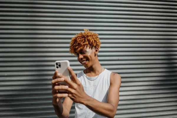 年轻的黑皮肤男子在街上摆姿势 并在城市背景下自拍 男人笑着在手机上拍照 幸福生活的概念 — 图库照片