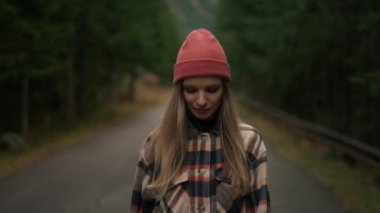 Sarışın kadın gezgin, doğa ile çevrili dağlarda yolda yürürken kameraya bakıyor. Seyahat gezisi seyahat tutkusu konsepti