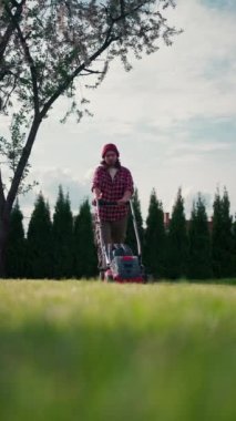 Vertical view of lawn-mover worker cutting green grass garden. Young man worker cutting grass with lawn mower alone