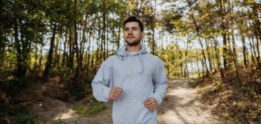 Erkek fitness modelinin portresi orman yolunda maraton antrenmanına hazırlanıyor doğa manzarasında koşucu adam orman yolunda koşuyor.