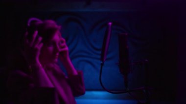 Ses kayıt stüdyosunda şarkı söyleyen yetenekli şarkıcı kızın portresi. Profesyonel kulaklıklı sakin bir kadın ve mikrofon stüdyoda neon ışıklı pop şarkılarıyla yeni bir albüm yaratıyor.