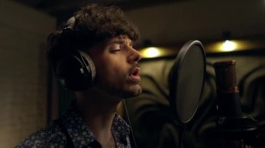 Şarkıcı profesyonel ses kayıt stüdyosunda yeni şarkı kaydediyor. Müzik ve ses kaydı için kulaklıklı ve mikrofon ekipmanlı bir adamın yakın plan portresi.