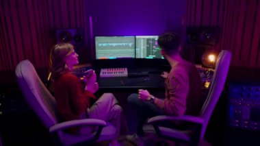 Genç müzisyen kadın yeni müzik kaydı sırasında ses operatörüne danışmanlık yapıyor. Her ikisi de ekran frekans dalgaları ve diğer ayarlar ve dinleme müzik ekipmanları ile otururken.