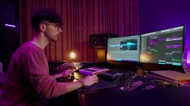 男性のサウンドエンジニア 音楽家は音楽を作成するためにMidiコントローラー デジタル電気ピアノを使用します サウンドトラックとソフトウェアインターフェイスを示すコンピュータ画面 録音スタジオ 音楽制作コンセプト — ストック動画