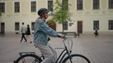 Sarışın, koruyucu kasklı, gülen bir kadın sokakta tek başına bisiklete biniyor. Bisiklet süren mutlu turistler. Seyahat, bisiklet kiralama, yaz konsepti.