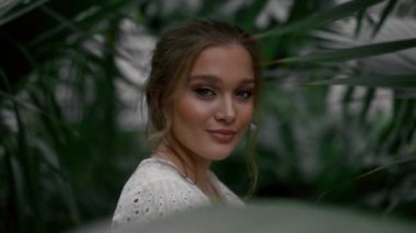 Botanik bahçesinde ya da konservatuarda kameraya poz veren beyaz elbiseli romantik genç bir kadın. Farklı bitki türlerini keşfediyor. Doğa ve insan kavramı