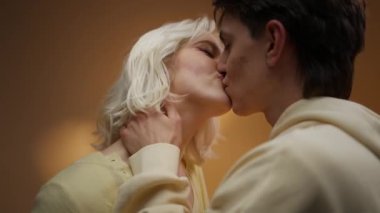 Tutkuyla öpüşen ve romantik bir randevu sırasında stüdyoda canlı turuncu bir ışık altında sevişmekten zevk alan genç ve güzel bir çift.