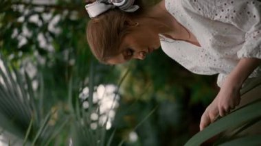 Eğreltiotu botanik bahçesinde dinlenen genç kadının dikey görüntüsü. Güzel bayan tropikal ağaçların tadını çıkarıyor.