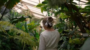 Arka planda, arka planda yeşil yapraklı ve beyaz camlı bir botanik bahçesindeki kız var. Mutlu kadın temiz havanın ve ormanların tadını çıkarıyor.