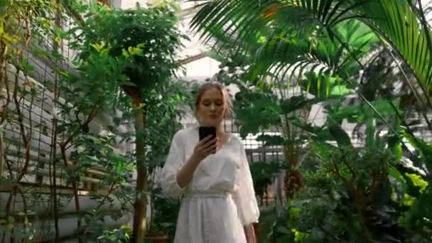 Молодая Мечтательная Женщина Ходит Мобильным Телефоном Ботаническом Саду Исследует Различные — стоковое видео