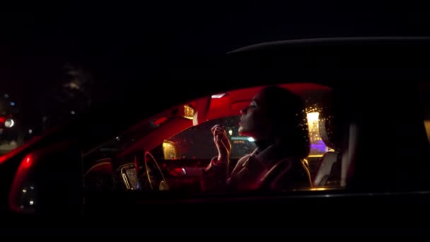 分散的司机 年轻迷人的女人在镜子里看着自己的嘴唇 晚上坐在车边化妆 — 图库视频影像