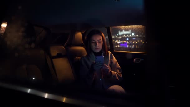 时尚奢华的女人穿着西服 晚上坐在乘客座位上的黑色轿车里 在旅途中看着她的智能手机 汽车商业概念 — 图库视频影像