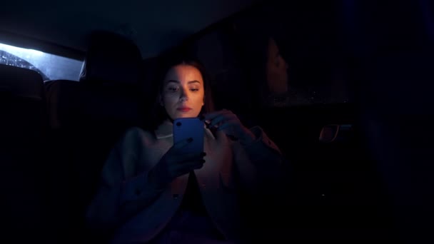 一位年轻貌美的女商人坐在汽车后座上 在城里的一场暴风雨中 她用手机看了看 — 图库视频影像