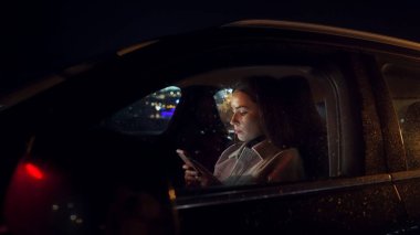 Odaklanmış iş kadını cep telefonunu sürücünün içinde kaydırıyor geceleri lüks bir araçla ofisten işe giderken oturuyor