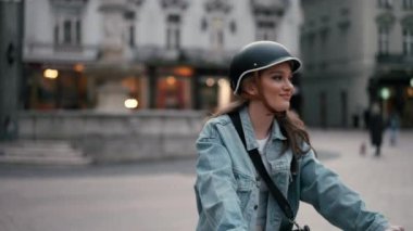 Şehir caddesinde bisiklet süren kasklı, uzun saçlı mutlu bir kadın. Açık hava portresi. Aktif yaşam tarzını seven güzel bir kadın. Rahatla konsept