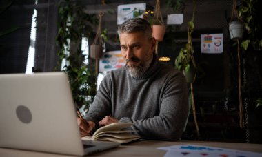 Modern ofis alanında çalışmak için bilgisayar kullanan şık günlük gömlekler giyen odaklanmış beyaz bir adam. Olgun ofis çalışanı e- postaları cevaplıyor, klavyeyi daktilo ediyor
