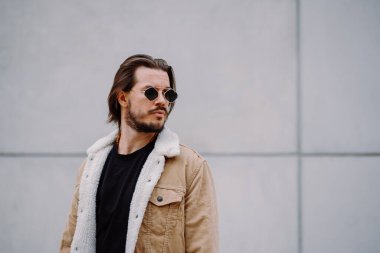 Şehir sokağında poz veren yakışıklı bir delikanlı. Yüzünde ciddi bir ifade var. Şık görünümlü çekici erkek hipster modeli.