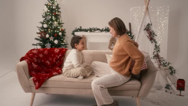シングルマザーは居間のクリスマスツリーの近くに座っている間に彼女の息子にプレゼントを与える クリスマスプレゼントを受け取る少年 ハッピーニューイヤーとメリークリスマスのコンセプト — ストック動画