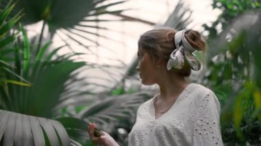 Botanik bahçesinde ya da konservatuarda beyaz elbise giyen genç bir kadın. Farklı bitki türlerini keşfediyor. Doğa ve insan kavramı