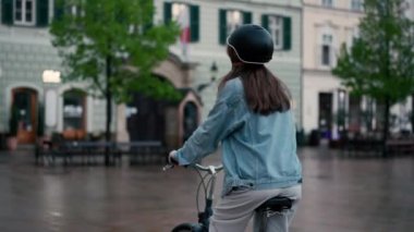 Şehir merkezindeki yağmurlu cadde boyunca bisiklet sürmekten hoşlanan güzel genç bir kadının arka manzarası. Etkin yaşam tarzı kavramı