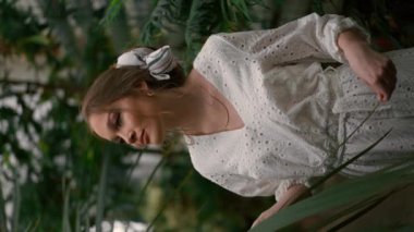 Eğreltiotu botanik bahçesinde dinlenen genç kadının dikey görüntüsü ve yavaş çekim görüntüsü. Güzel bayan tropikal ağaçların tadını çıkarıyor.