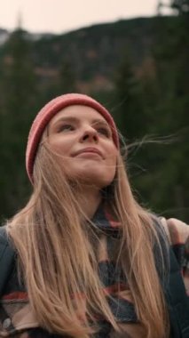 Blonde tourist woman gazing at mountains and lake. Caucasian girl with hat and backpack looking at scenic views alone. Travelling concept