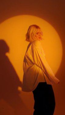 Blonde-haired joyful girl in white shirt dancing with inspired face expression. Active young woman in casual summer outfit having fun indoor