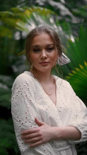 バックグラウンドに熱帯の木で植物園でポーズする若い夢見る女性の垂直な眺め ジャングルコンセプト — ストック動画