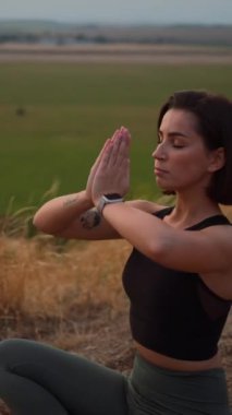 Calm serene sporty young woman meditate while sitting in namaste pose with eyes closed. Girl doing breathing exercises practice while relaxing outdoor