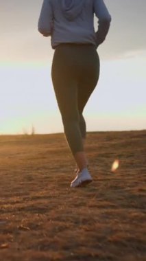 Closeup view of the strong woman running on a rural field at sunset during the summer. Healthy sport lifestyle concept