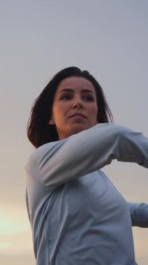 Woman standing and warming up while making preparation for a jogging run. Girl twisting on a high cliff with cloudy sky in the background