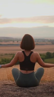 Athletic lady is doing fitness among green wild nature. Woman sitting in the lotus pose and using yoga practices. Relaxing outside concept