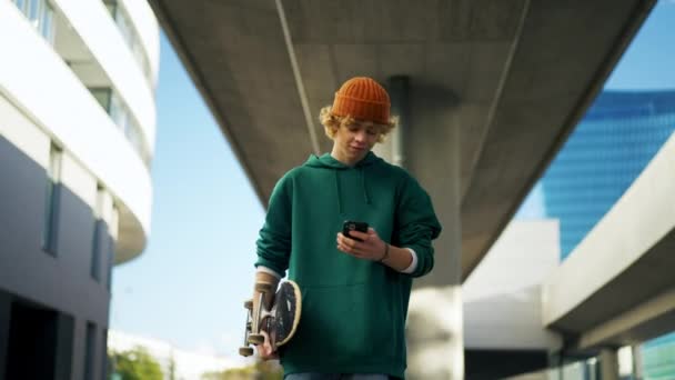 Улыбающийся Студент Смотрит Мобильный Телефон Гуляет Городу Крупным Планом Скейтер — стоковое видео