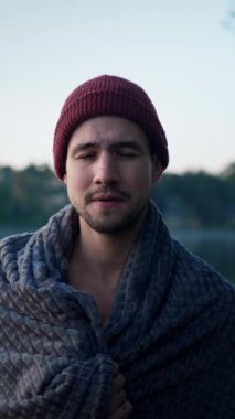 Portrait view of the bearded man wrapping at the towel feeling cold and chills after the winter swimming at the cold huge lake at the forest. Morning sunrise at the background