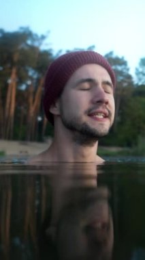 Portrait of the serious man swimming in ice lake during winter morning. Male person feeling cold and showing his emotions. Healthy lifestyle concept