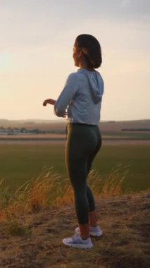 Young sporty woman in sportswear stretching on hill top, warming up or doing yoga on cloudy sky background. Fitness, healthy way of life, wellbeing, freedom, loosing weight concept