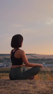 Healthy lifestyle. Young caucasian woman practicing yoga outdoors while sitting at the hill at the lotus pose. Harmony and meditation concept