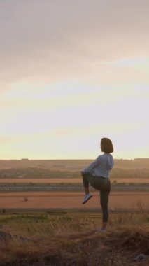 Female runner warming-up her legs on a high mountain during the sunset. Girl in happy mood training at the open air