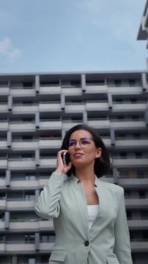 Female realtor wearing formal suit holding smartphone while going through the financial district. Businesswoman near the road in the urban space