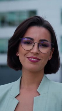 Smiling caucasian young woman in formal outfit looking to camera outside on street while feeling happy. Portrait of business modern manager showing sincere emotions