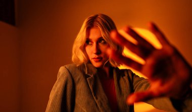 Güneş gözlükleriyle poz verirken dans eden kadın portresi. Kadın model, neon turuncu arka planda ceket giyiyor. Moda konsepti 