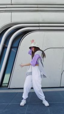 Dışarıda dans eden güneş gözlüklü, şapkalı ve kameraya bakan modacı kadın. Dans gösterisi yapan kadın dansçı serbest stil dublörlüğü yapıyor. Komik, şık, beyaz, hip hopgirl. Yüksek kalite 4k görüntü