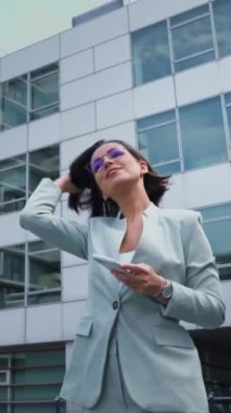 Low angle view of the confident businesswoman using smartphone while going through the street. Happy lady making work call in the urban space